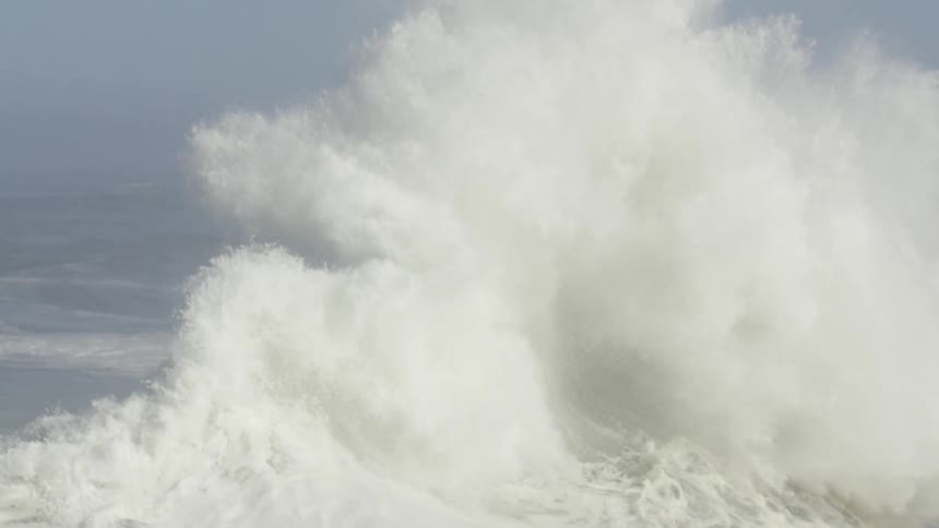 Waves on a stormy sea crashing into each other and spraying sea water hundreds of feet into the air