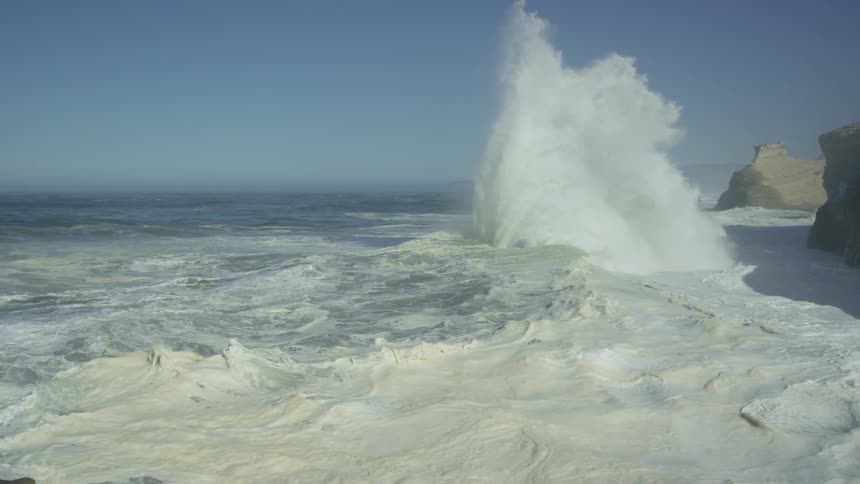 Camera lift revealing massive waves colliding and exploding on a sunny coastal ocean day