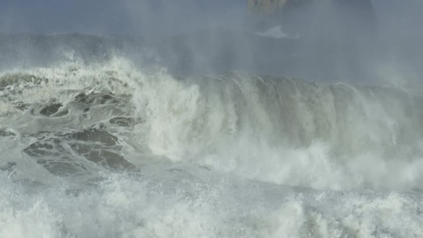 Large waves crashing against each other in front of a large boulder