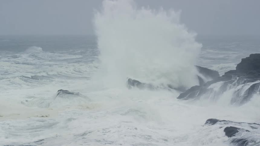 Waves crashing, spraying, and foaming on the rocks of a shoreline