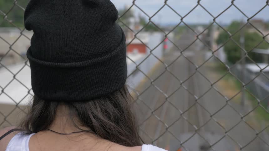 A woman looks out the fence on an overpass over the train