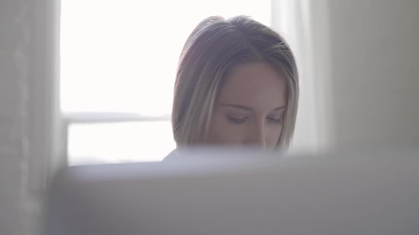 Blonde woman types on keyboard in front of window during daylight