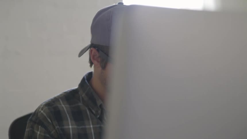 A man wearing a backwards ball cap types at a computer