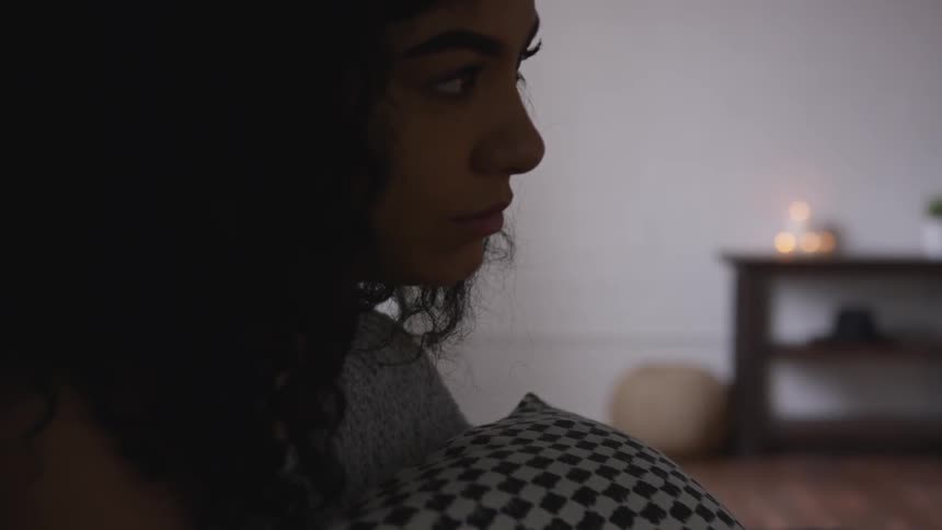 A black woman holds a pillow and looks across the room