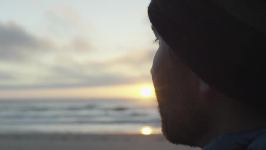 Man on a beach watches the sunset