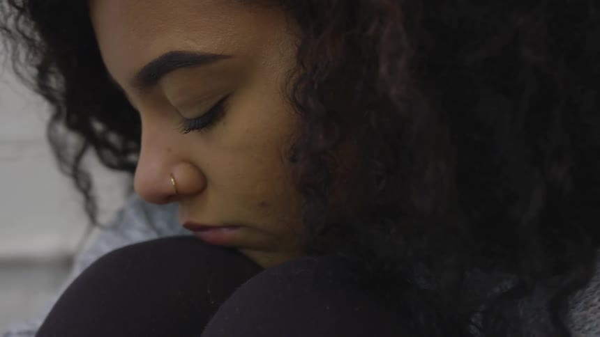 A young girl with curly hair sits with her head pressed to her knees