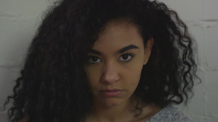 A woman with curly black hair and a nose piercing looks up