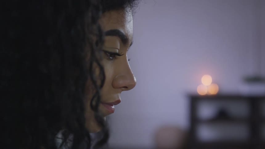A black woman sits in a room and looks down at an object