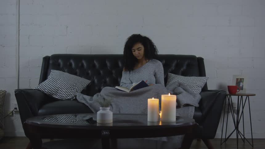 A woman sitting on a black sofa reading a book