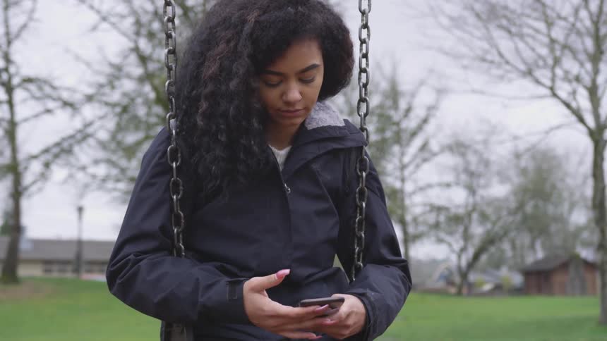 A girl sits on a swing and checks her phone