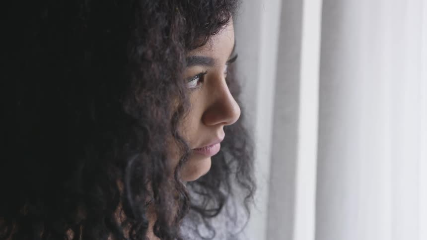 Young woman appears to be nervous and afraid looking out the window