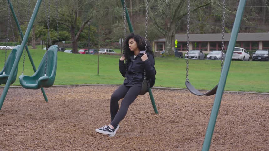 A young woman sits on a swing in a park