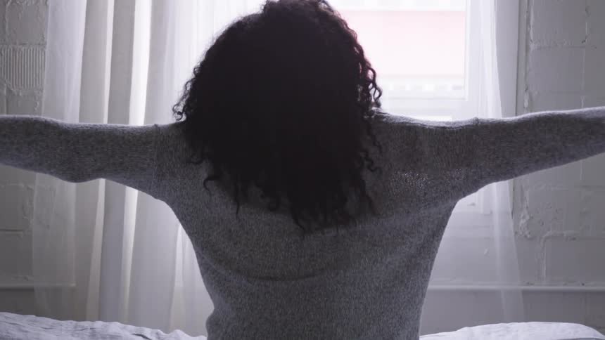 A black woman stretches while sitting in bed
