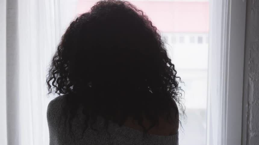 A woman stands and looks out a window