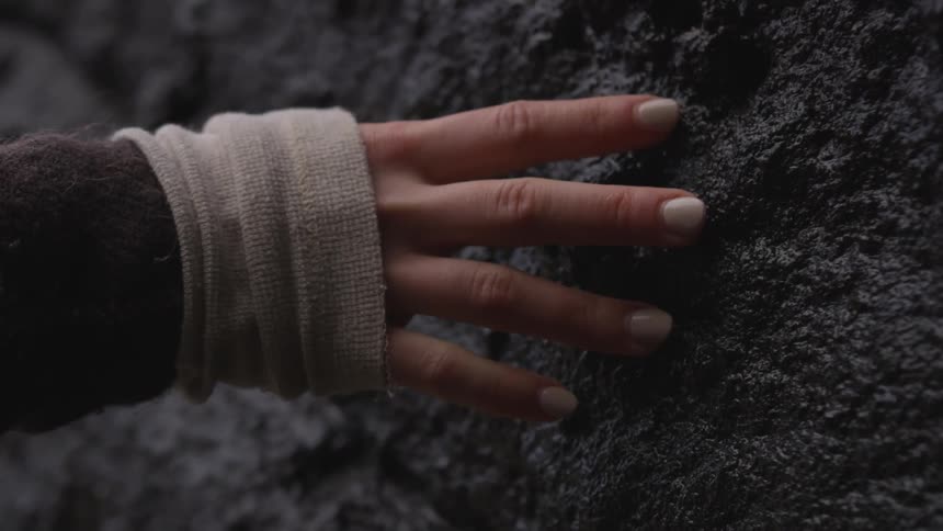 Woman's hand touches the dark rock during daylight