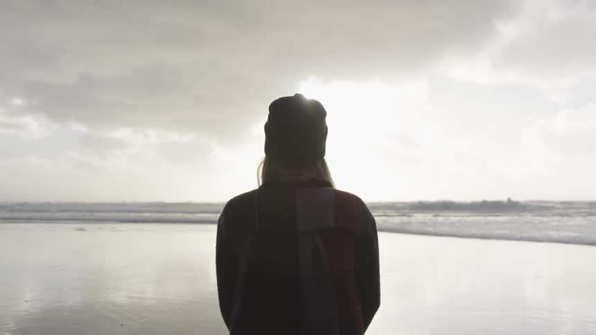 A woman looks out over a body of water as she stands by the shore