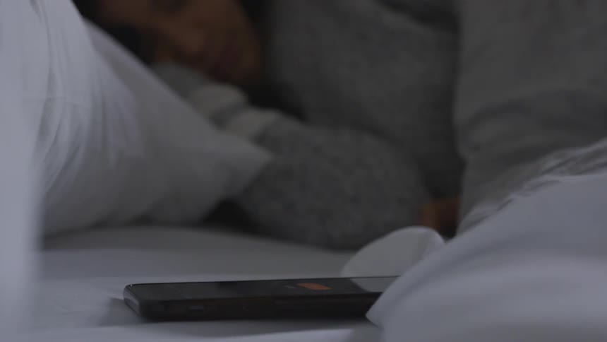 Woman sleeps in bed while smartphones alarm goes off in bedroom in the morning