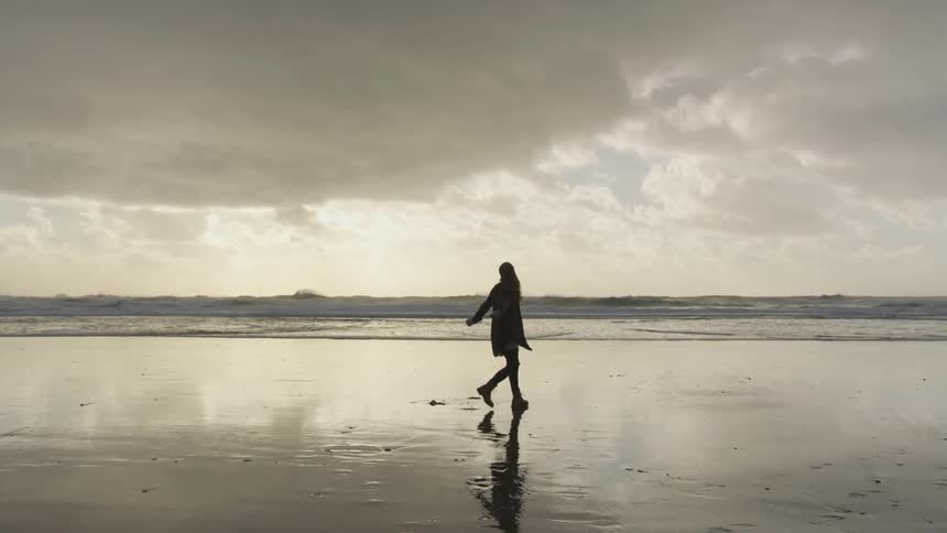 A woman twirls on the wet sand of the beach with her arms outstretched
