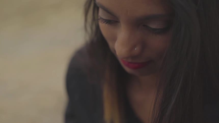 A woman with a nose ring looks down and smirks