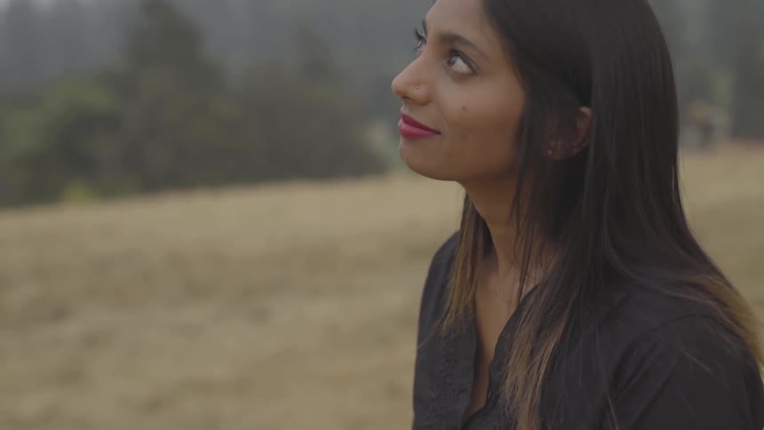 An indian woman looks up and smiles while standing outdoors