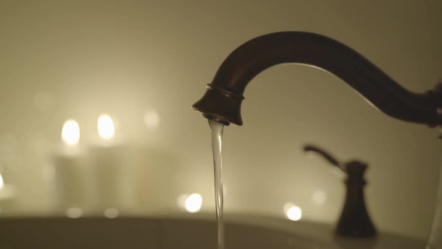 Water runs from a faucet as candles glow in the background