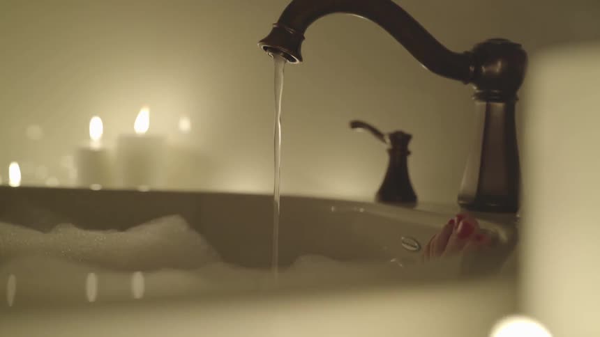 Water flows from the tap into the bubble bath as candles burn nearby