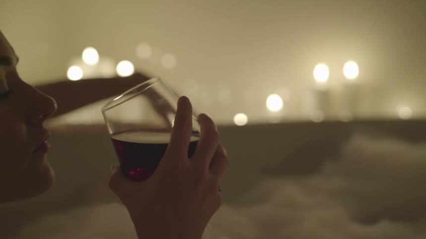 A white woman in a bathtub sips some red wine