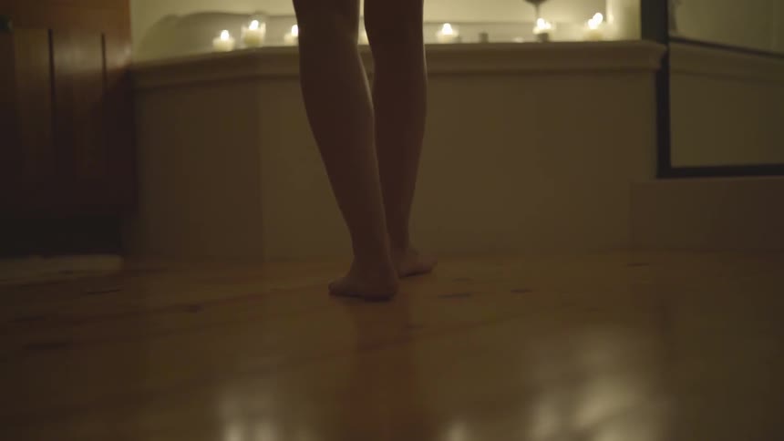 Bare feet woman walks towards bathtub with burning candles on it in bathroom