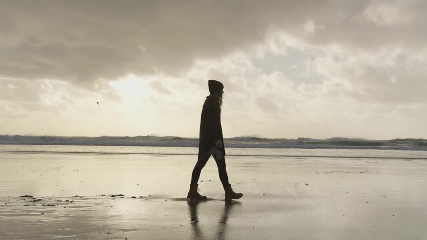 A woman walks along a beach in boots in low tide