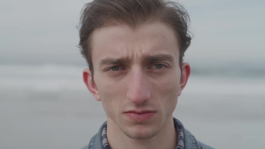 A man slowly looks up as he stands with his back to the ocean