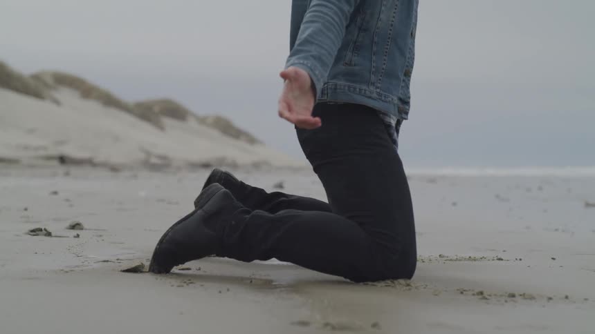 A man kneels down on the beach sand