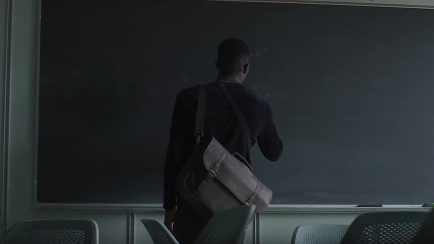 A man writes math problems on a chalkboard