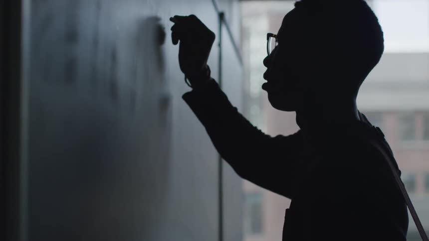 A man is writing on a chalkboard in a dark room