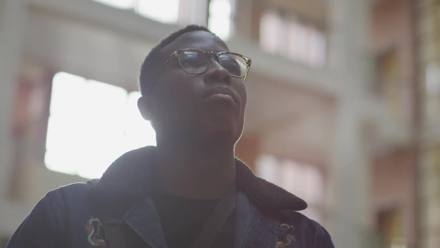 A black male in eyeglasses standing near buildings