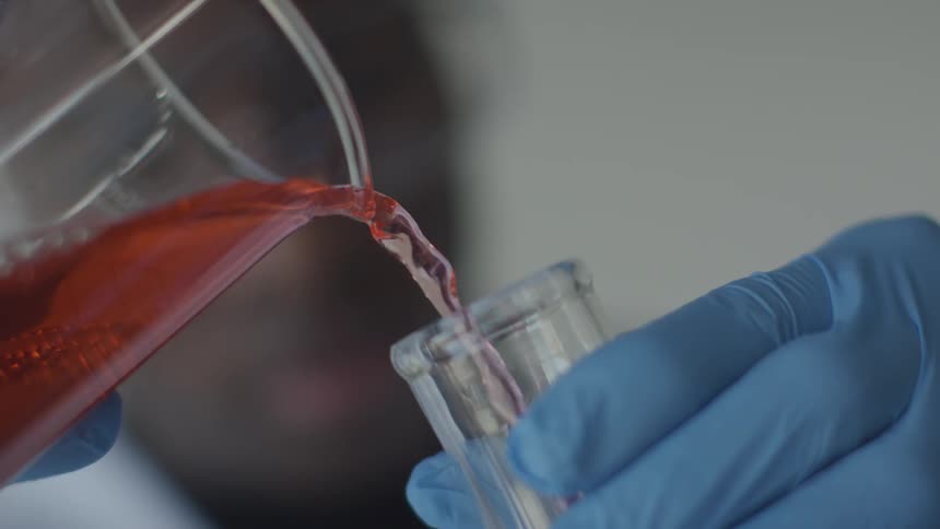 Someone pours red liquid from a beaker into a test tube