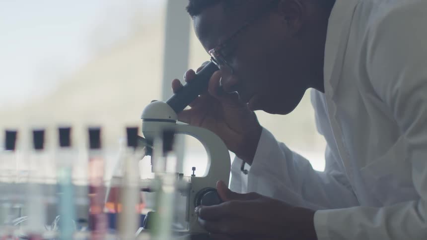 Main a white lab coat looks in a microscope