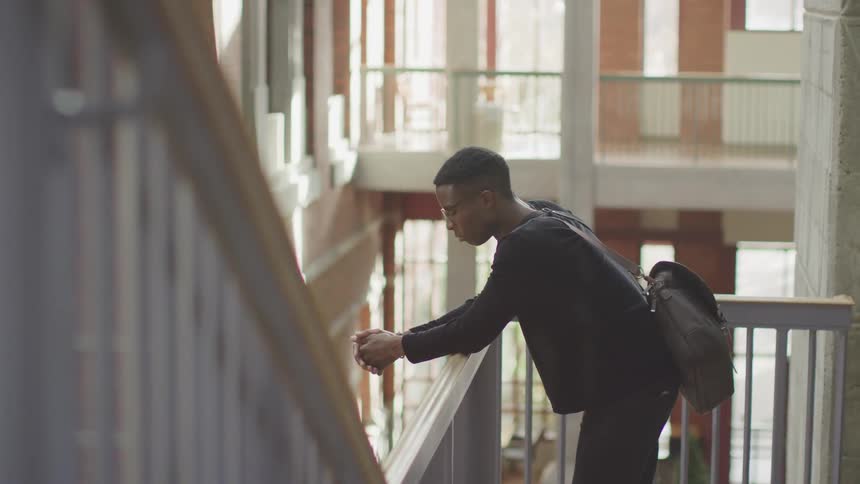 A man standing at a railing near stairs in a building