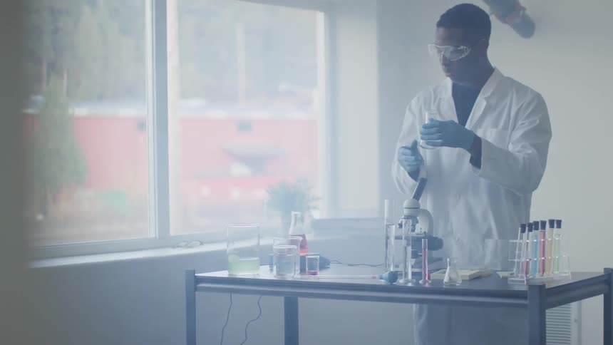 A man with goggles pours a solution in to a beaker