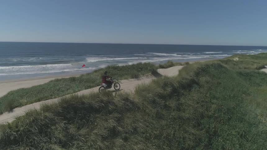 A person rides a motorcycle up a trail at the beach
