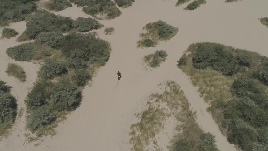 A person rides a dirt bike across sand