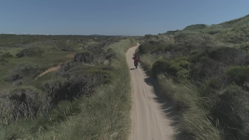 A man riding a motorbike down a grass lined dirt path