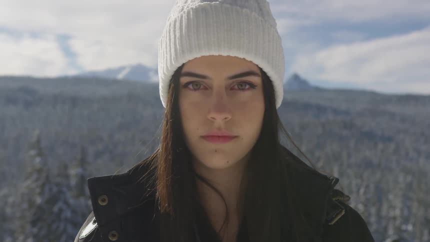 A woman stands in a wide open field in front of mountains