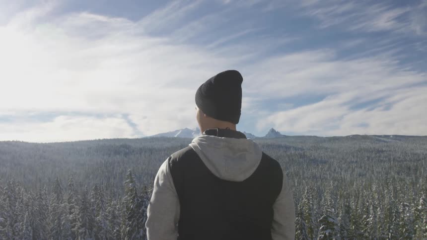 A man looks out across a snowy forest from an elevated location