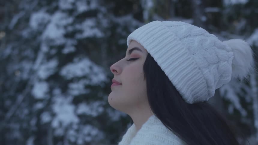 Woman stands in the snowy forest with her eyes closed