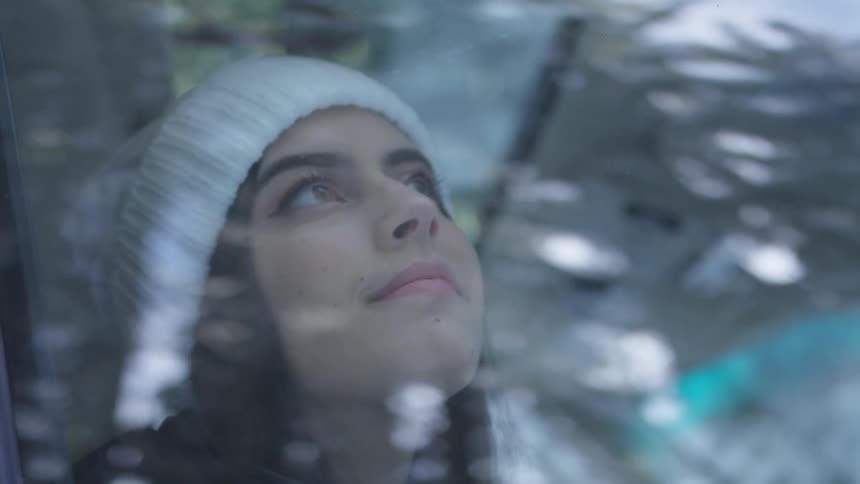 Woman wearing wooly hat looks up happily from a car during light