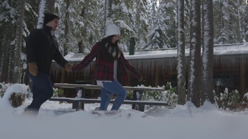 A man and a woman are holding hands while walking in a snowy forest