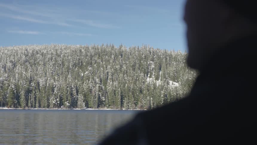 A man staring at snow covered pine trees along a river