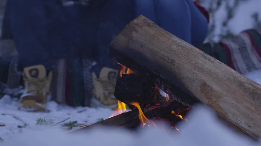 People sit near wood fire outdoors