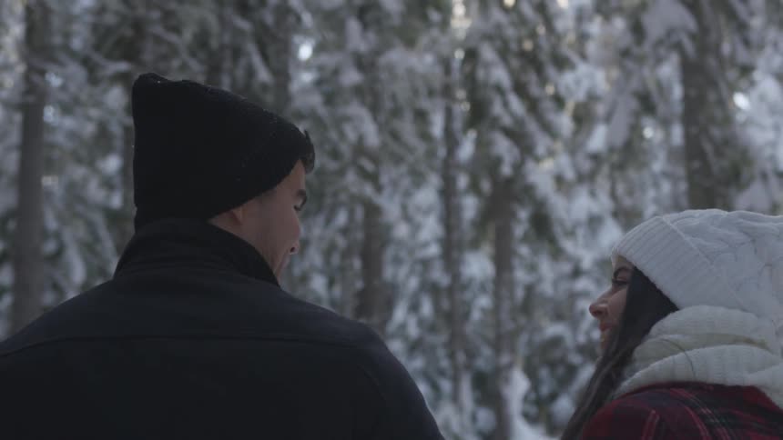 Man and woman wearing winter clothes walk down in the snowy forest by day