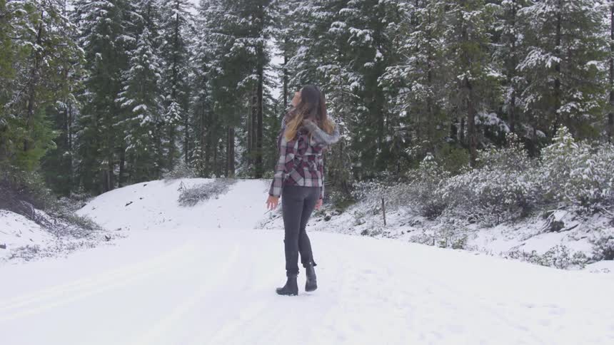 A young woman walking down a snowy path and playing with snowflakes on a winter day